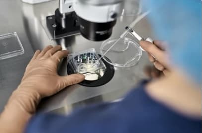 Embryologist's gloved hands with a pipette and culture dish at a microscope